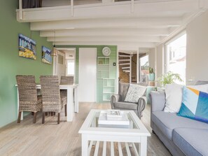 Een woonkamer met een bank, een salontafel, rieten stoelen, een boekenkast en een trap.