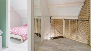 A bedroom with a bed, a large mirror, a staircase, and a brick wall. - Vacation Home 450 m From the Beach (Katwijk Aan Zee)
