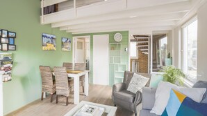 A spacious living area with a dining table and chairs, a sofa, and a coffee table. There is a staircase leading to an upper level. - Vacation Home 450 m From the Beach (Katwijk Aan Zee)
