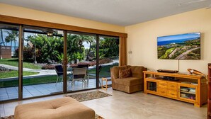 Un salón espacioso con un gran ventanal corredera que da a un jardín, un sofá cómodo, un mueble de madera y un cuadro de un paisaje.