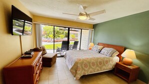 Habitación de hotel con cama, escritorio, silla, televisor y ventana con vistas a zonas verdes.