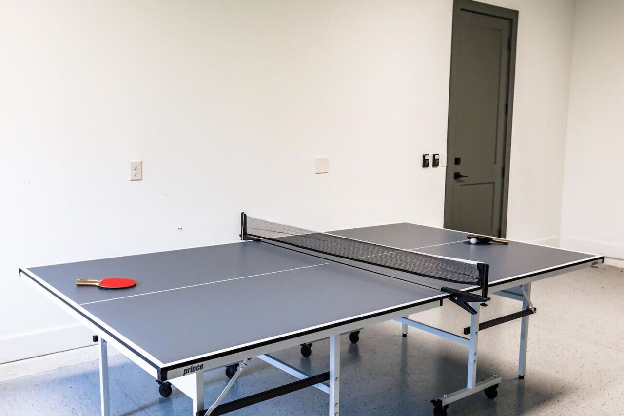 Ein Tischtennis-Tisch mit einem roten Schläger, eine Tür und ein Lichtschalter an der Wand.