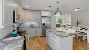 A modern kitchen with white cabinets, a central island, and a dining area with a white table and chairs.