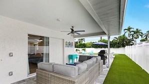 A covered patio with a wicker sofa, a grill, and a pool table.