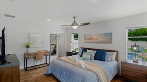 A bedroom with a bed, bedside tables, a desk, a chair, a ceiling fan, and artwork on the walls.
