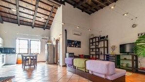 A spacious living area with a high ceiling, a sofa, a television, and a kitchen in the background. - Welcomely- In Barberia Milis (Milis)