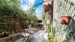 A narrow outdoor patio with a wooden table and chairs, surrounded by lush greenery and cacti. - Welcomely- In Barberia Milis (Milis)