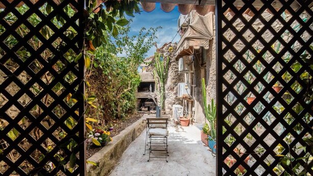 A narrow alleyway with a metal chair, potted plants, and a building with a stone facade. - Welcomely- In Barberia Milis (Milis)