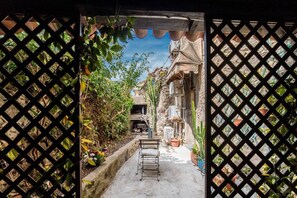 A narrow alleyway with a metal chair, potted plants, and a building with a stone facade. - Welcomely- In Barberia Milis (Milis)