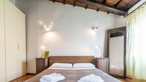 A neatly made bed with two pillows and folded towels, a bedside table with a lamp, and a mirror on the wall. - Welcomely- In Barberia Milis (Milis)