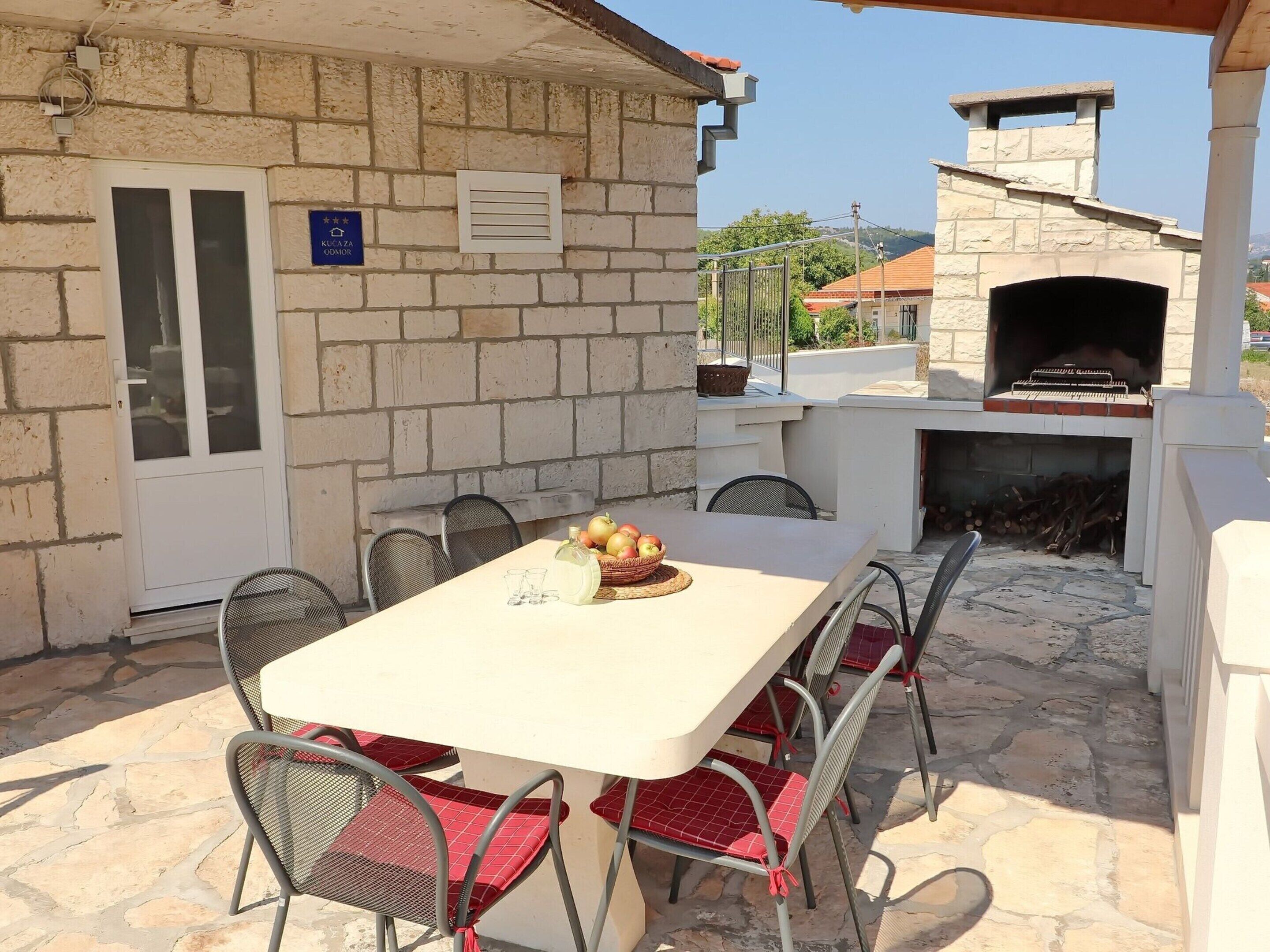 An outdoor dining area with a stone wall, a grill, and a view of the surrounding neighborhood.