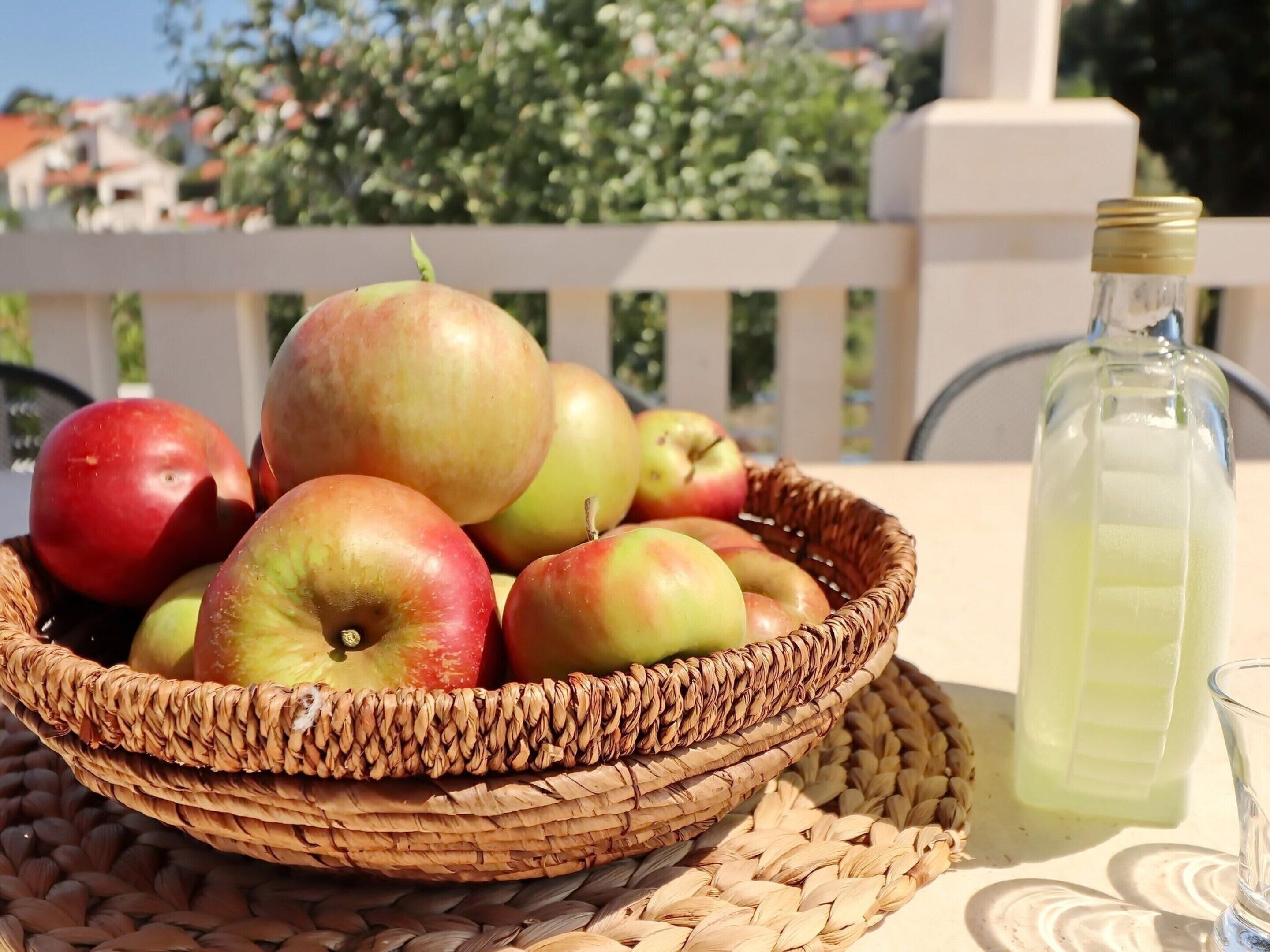 A wicker basket filled with apples on a table with a glass and a bottle of water.