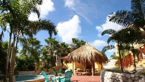A pool area with stone walls, a thatched-roof structure, and green chairs. - Air-conditioned Mama Sha Apartment Near Jan Thiel (Jan Thiel)
