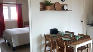A room with a bed, a dining table with chairs, a small kitchen area, and a wall-mounted clock. - Air-conditioned Mama Sha Apartment Near Jan Thiel (Jan Thiel)