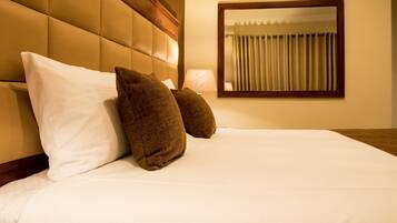 A neatly made bed with white and brown pillows, a wooden headboard, and a mirror on the wall.