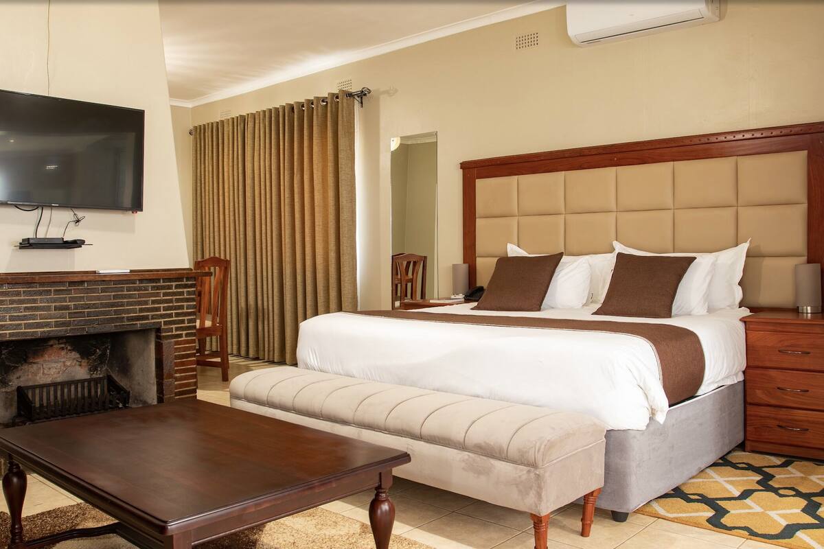 A hotel room with a bed, a TV, a fireplace, a wooden table, and a sofa.