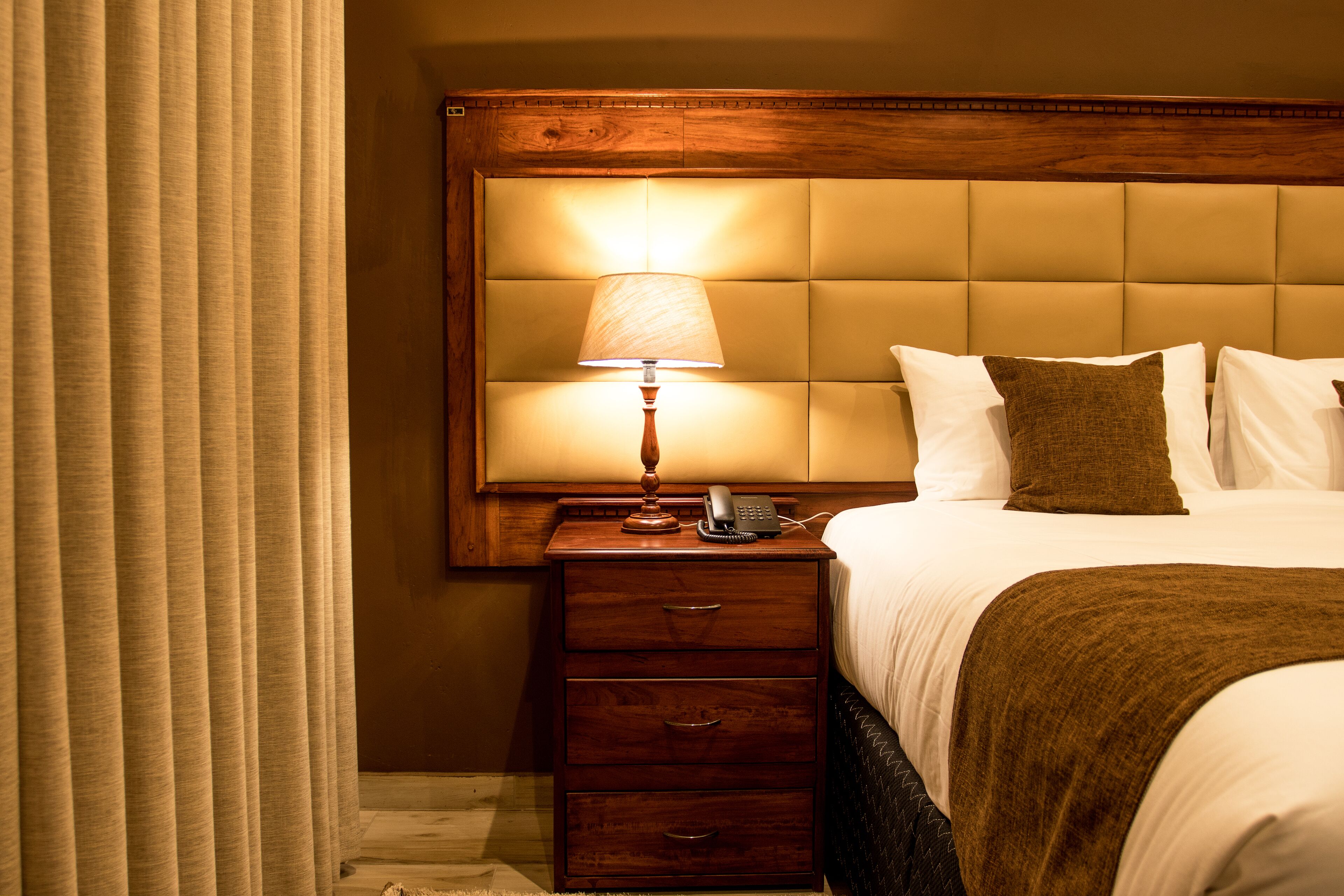 A hotel room with a wooden headboard, a bedside lamp, a telephone, and a brown throw blanket.