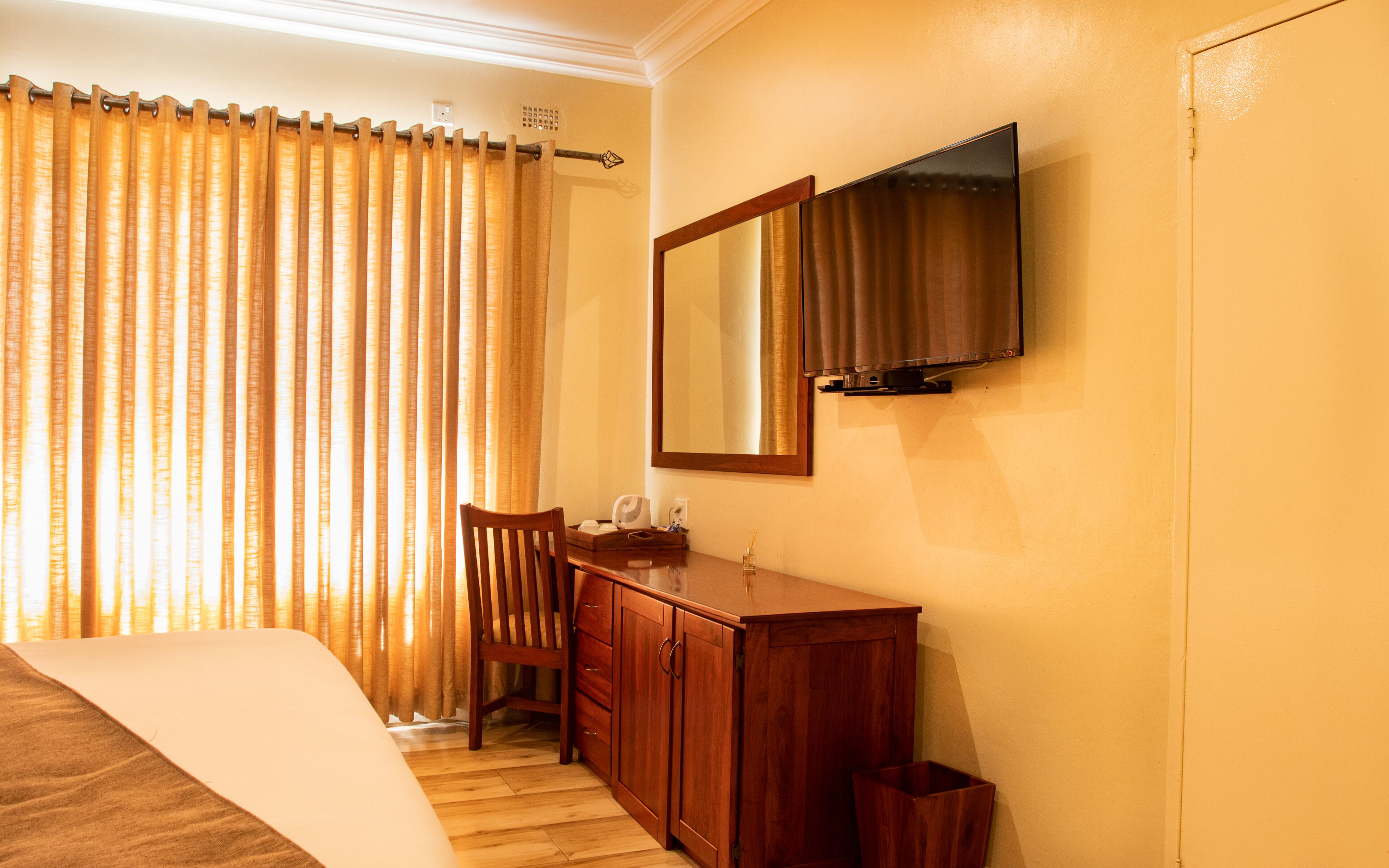 A hotel room with a bed, wooden desk, mirror, and a television on the wall.