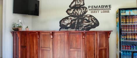 A reception desk with a wall-mounted TV, a refrigerator stocked with beverages, and a wall art piece.