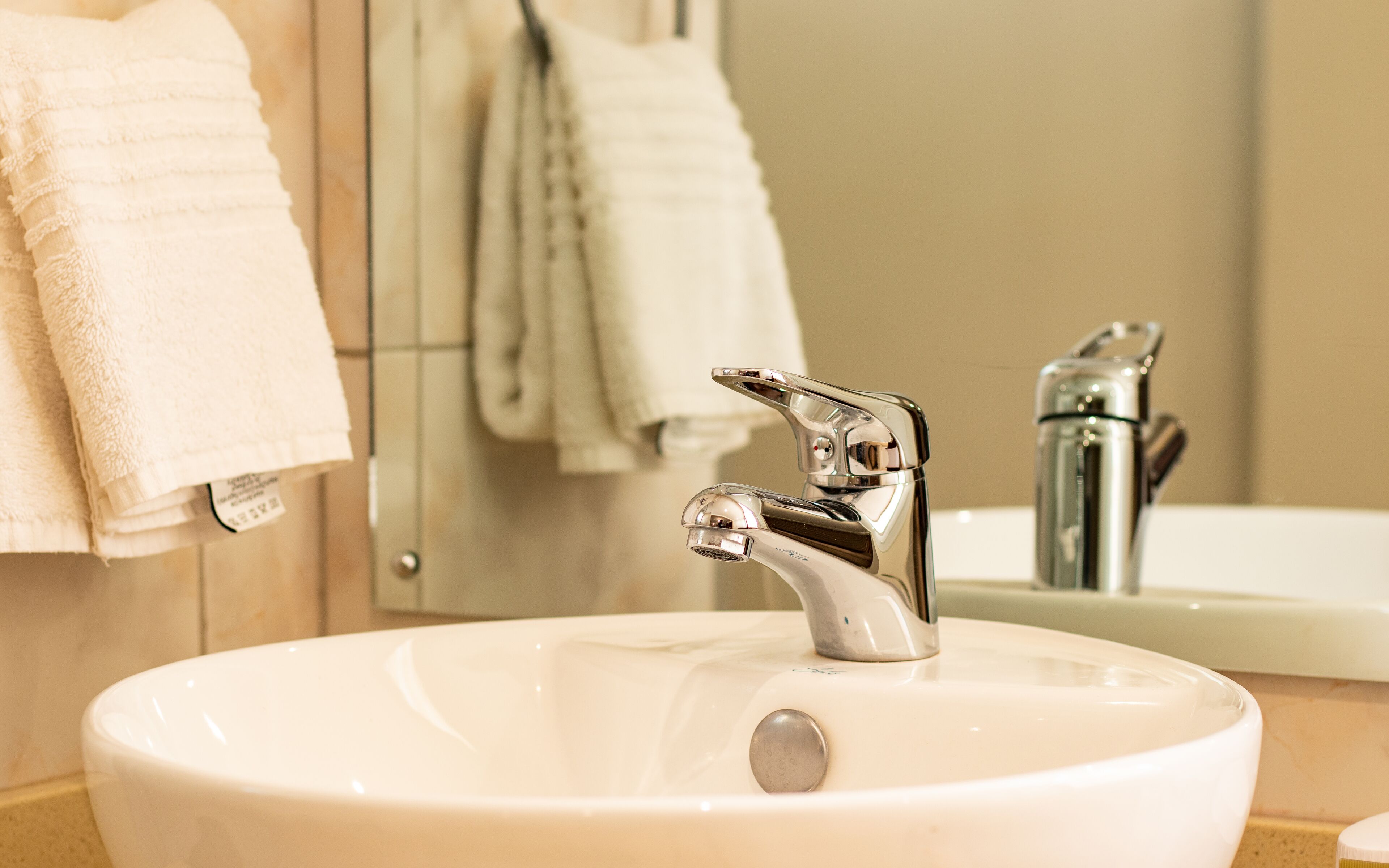 A bathroom sink with a chrome faucet, a mirror, and hanging towels.