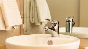 A bathroom sink with a chrome faucet, a mirror, and hanging towels.