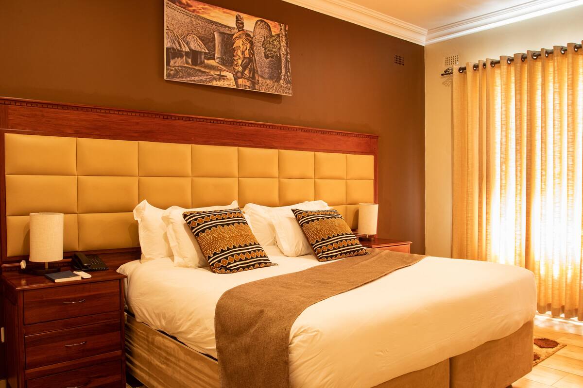A hotel room with a large bed, wooden headboard, and a painting above it.
