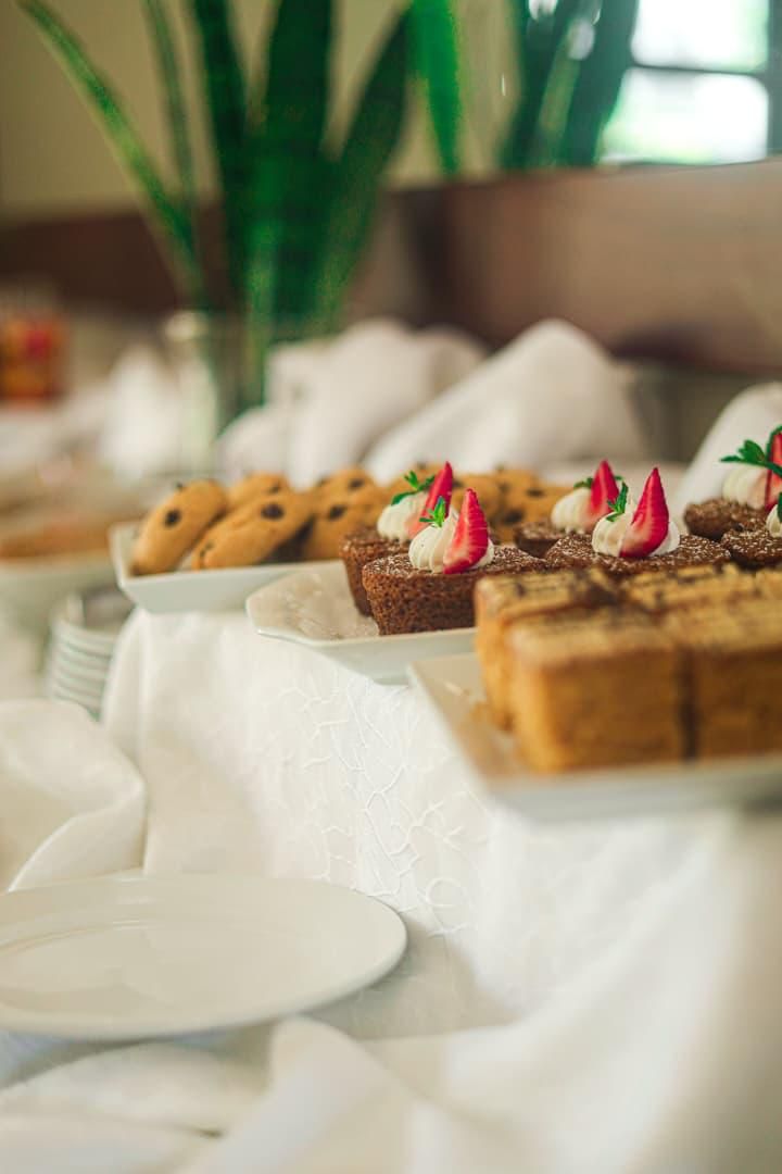 A table with desserts, including cookies and a cake, with a white tablecloth and a plant in the background.