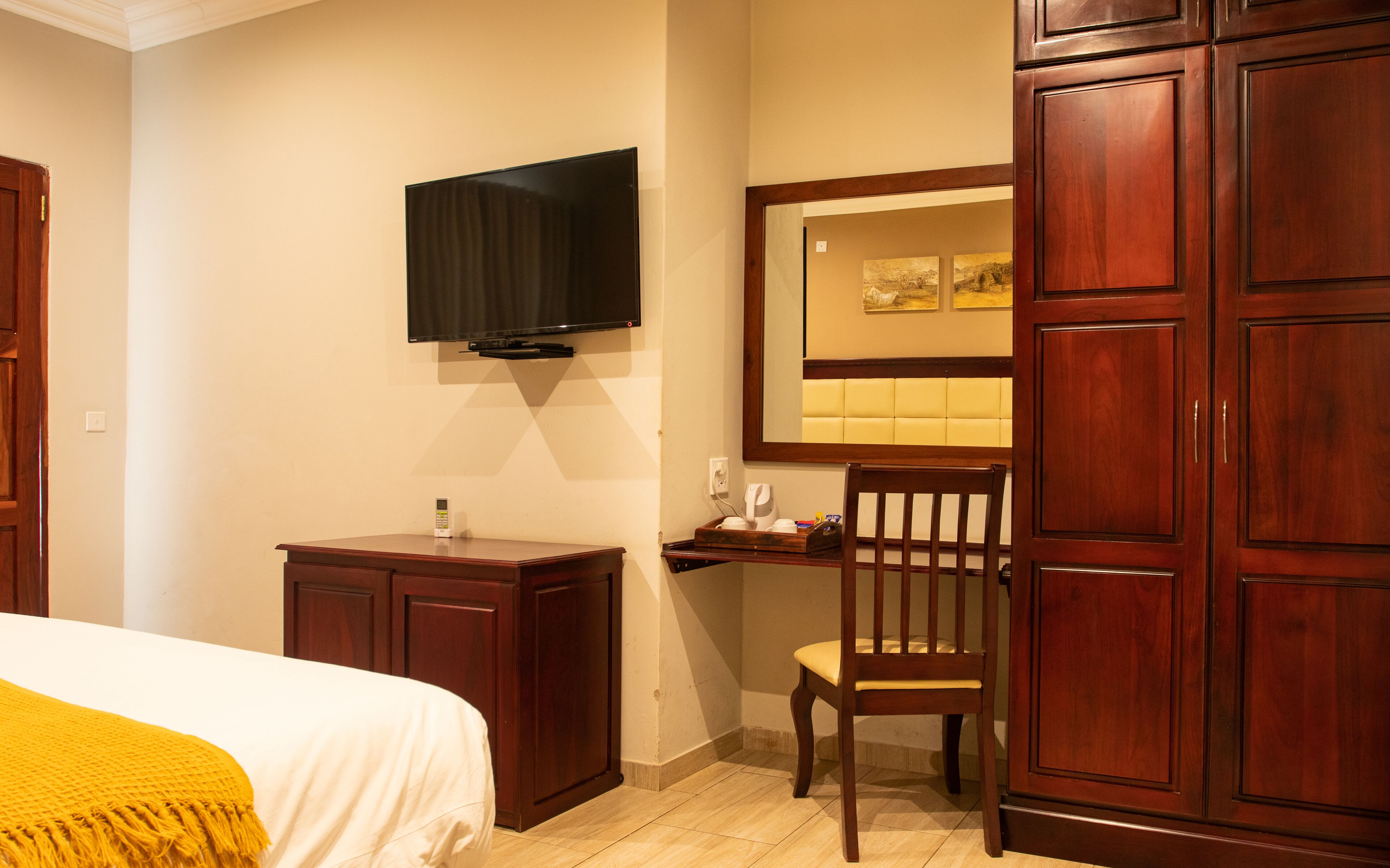 A hotel room with a bed, a desk, a chair, a television mounted on the wall, and a large mirror.