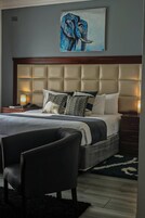 A modern bedroom with a tufted headboard, a large bed with multiple pillows, a bedside table with a lamp, and a chair.