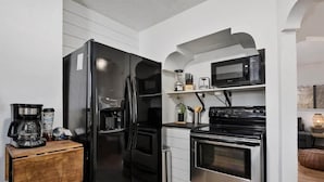 A compact kitchen with a black refrigerator, a microwave, and a stove. There is a wooden counter with a coffee maker and a blender. - #StayinMyDistrict TwinFalls Tudor (Twin Falls)