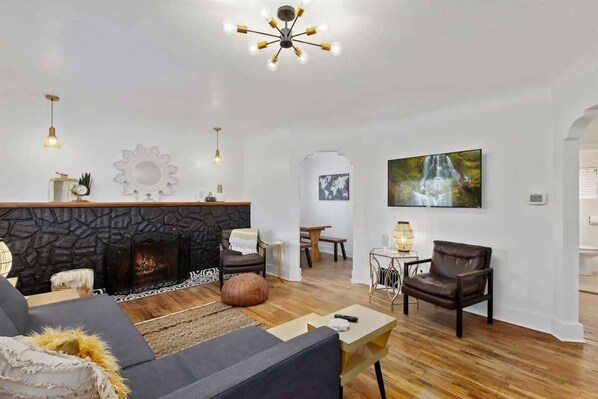 A modern living room with a stone fireplace, a large painting, and a chandelier.