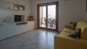 A modern living space with a sofa, a TV, a kitchen area, and a sliding glass door leading to an outdoor patio.