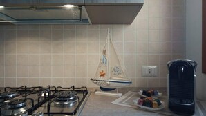 A kitchen with a gas stove, a hanging sail decoration, and a kettle on the counter.