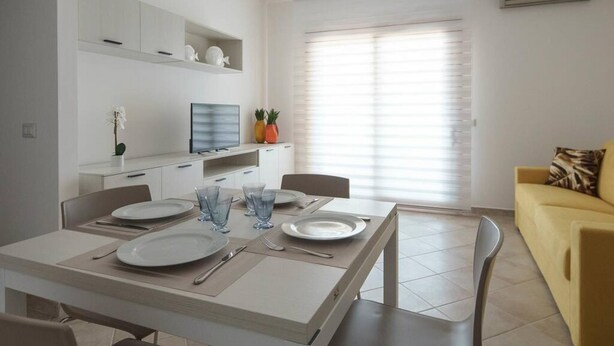 A modern dining area with a white table set for four, a sofa, and a TV on a white cabinet.