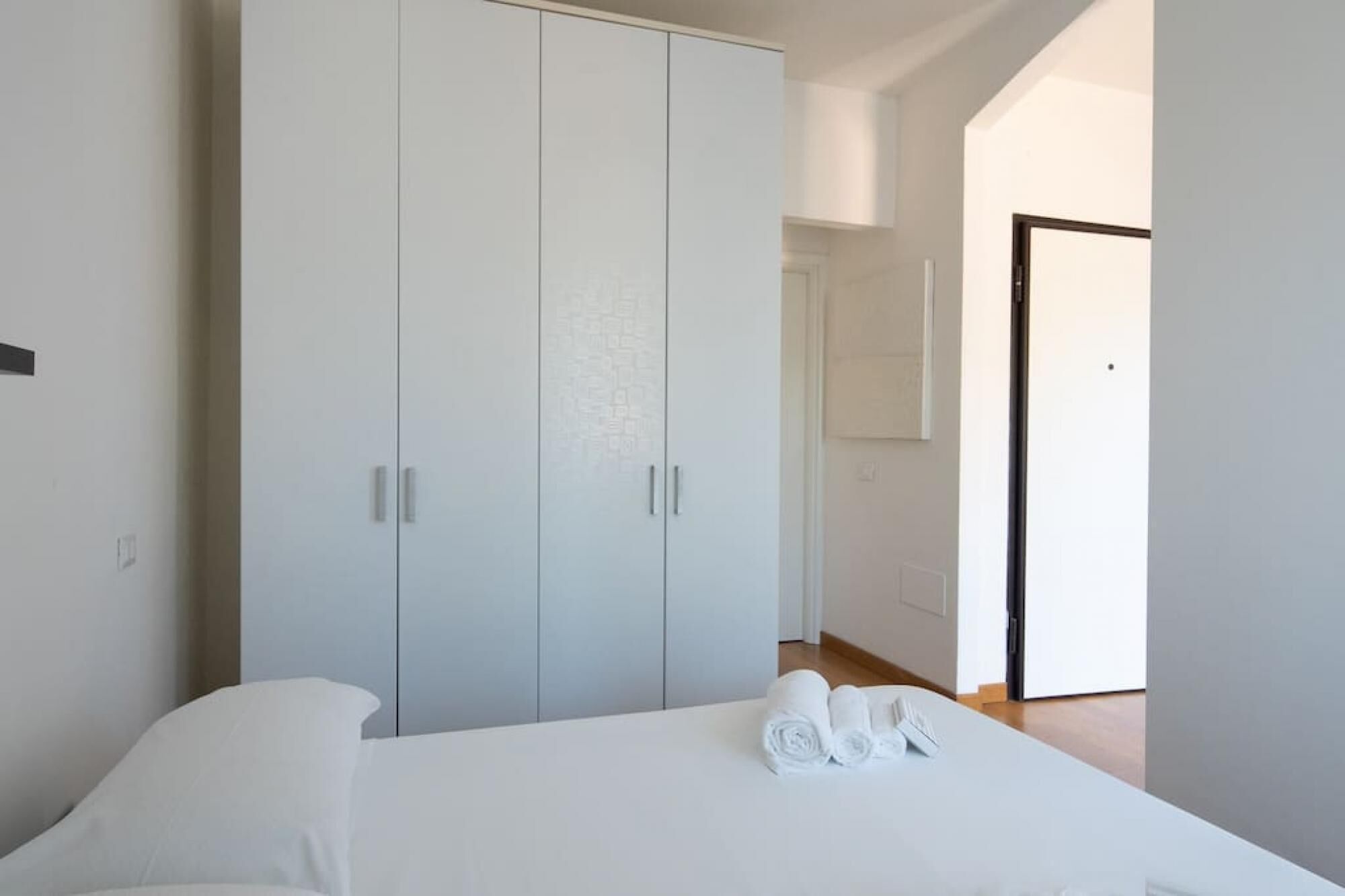 A bedroom with a large wardrobe, a neatly made bed, and a view of a hallway.