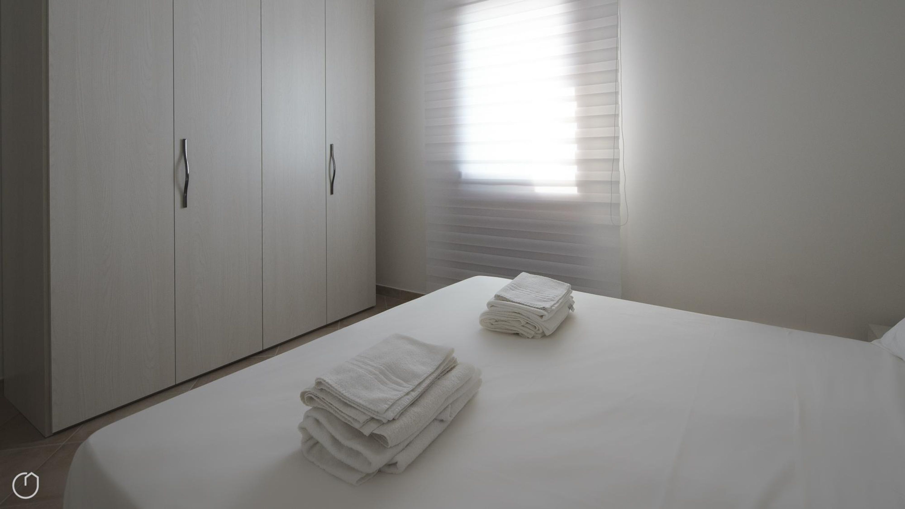 Een minimalistisch slaapkamer met een groot bed, twee stapels netjes gevouwen handdoeken en een kast met een handgreep.