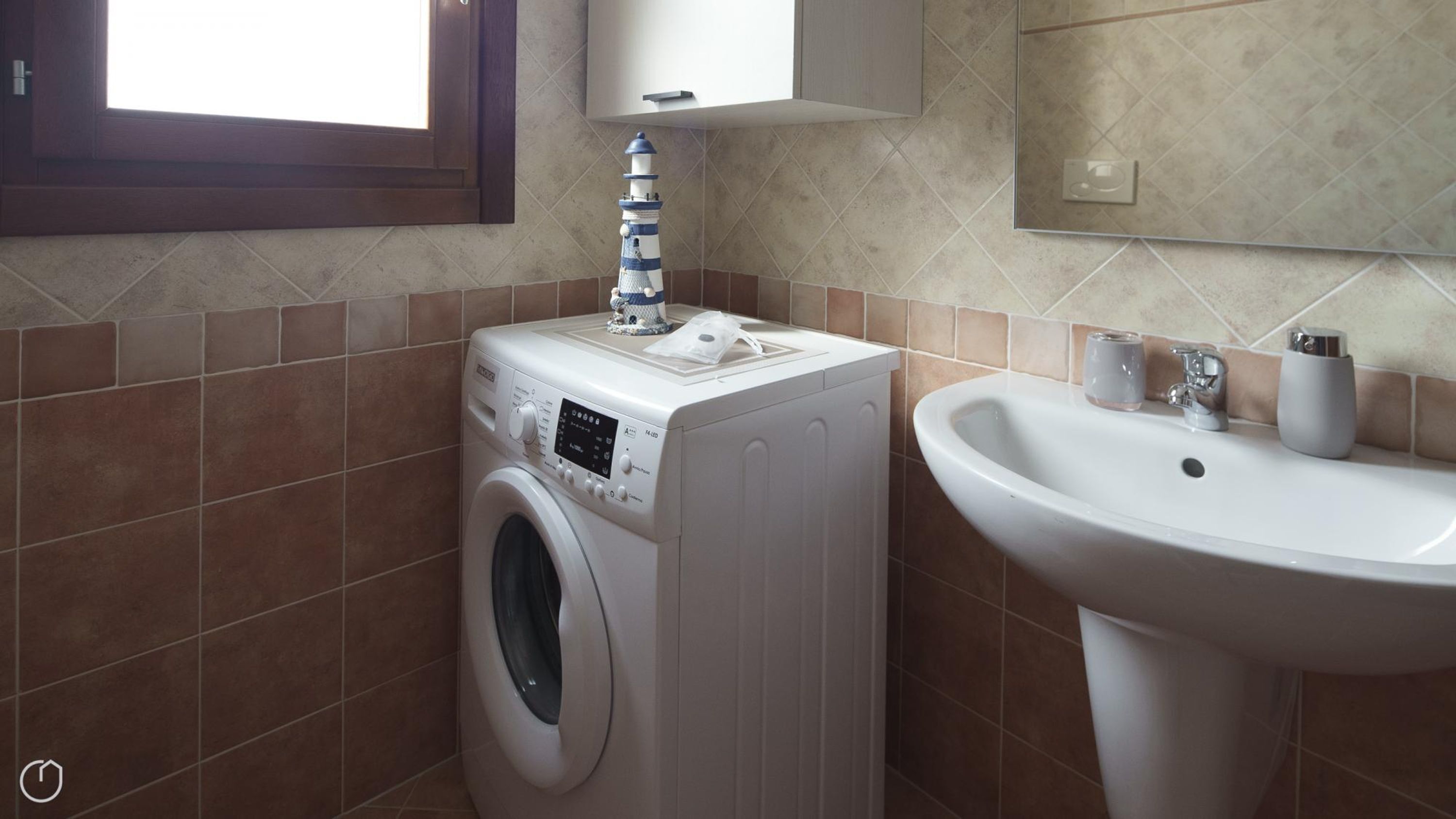 A compact bathroom with a washing machine, a sink, and a small window.
