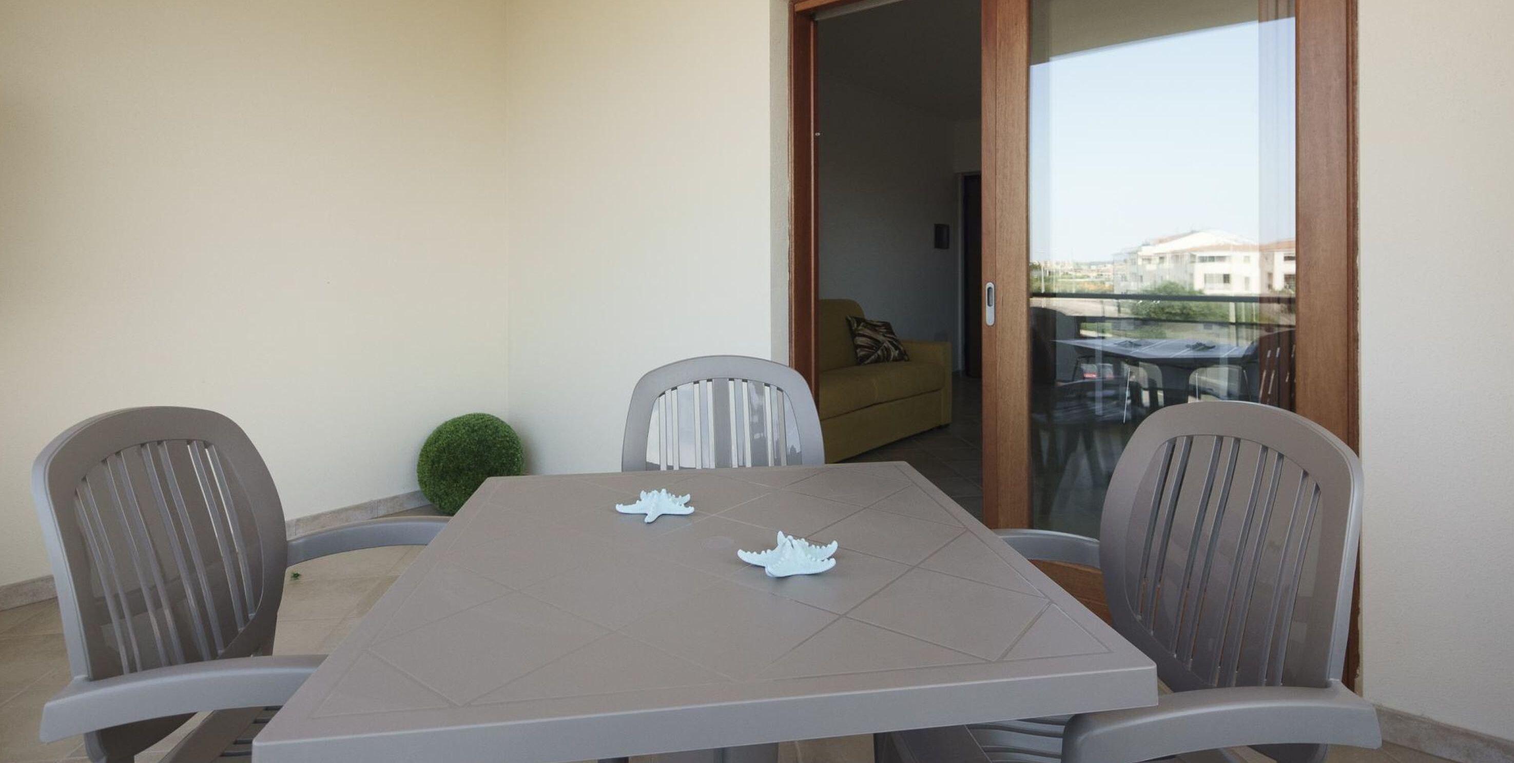 A balcony with a table and chairs, a small potted plant, and a view of buildings in the background.