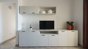 A modern living room with a flat-screen TV, a small white orchid, and decorative fish figurines on a light-colored cabinet.