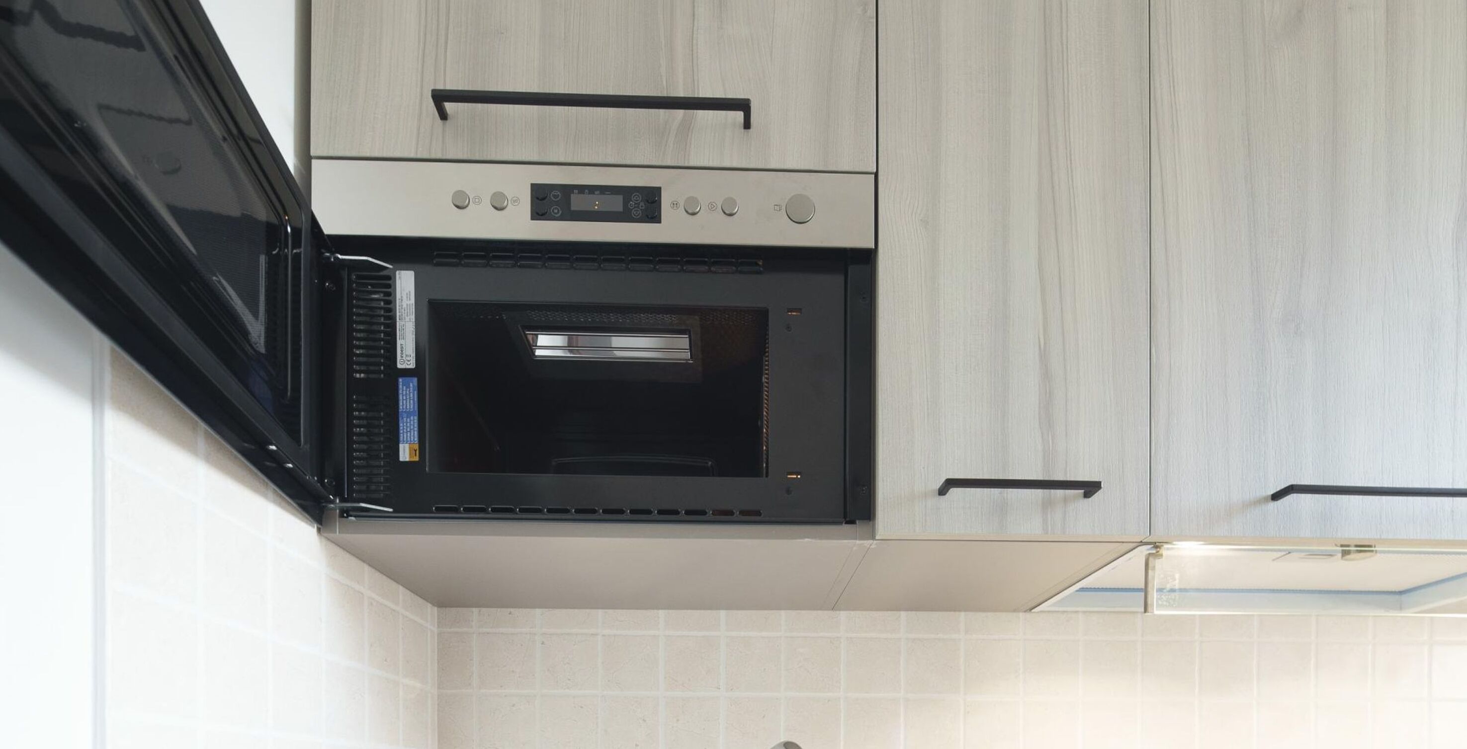 A kitchen with a built-in oven, light wood cabinetry, and a tiled backsplash.