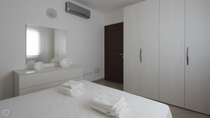 A modern bedroom with a large bed, a dresser, a mirror, and a wardrobe.