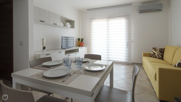 A modern kitchen with white cabinets, a dining table set for four, and a yellow sofa in the living area.