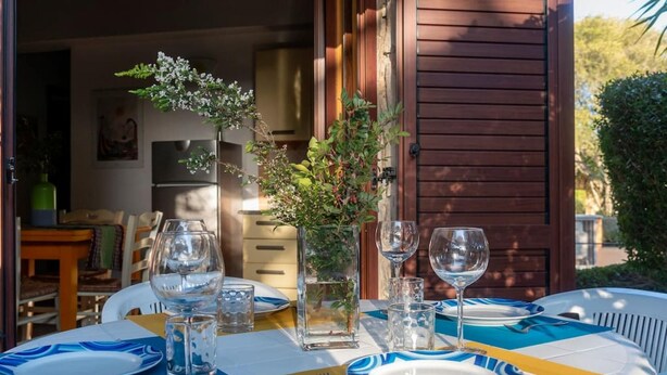 Un espace de restauration en plein air avec une table dressée pour quatre personnes, agrémenté de verres transparents et de vaisselle bleue et jaune.
