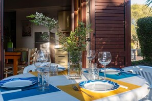 An outdoor dining area with a table set for four, featuring clear glassware and blue and yellow tableware.