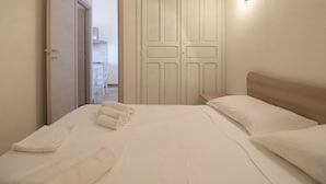 A neatly made bed with white linens and two rolled towels, a wooden headboard, and a white door with a handle. - Welcomely - Villa Paola B (Muravera)
