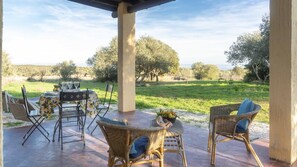 An outdoor patio with wicker furniture, a table set with glasses, and a view of a grassy landscape with trees. - Casa Oliveto 1 in Galtell (Galtelli)