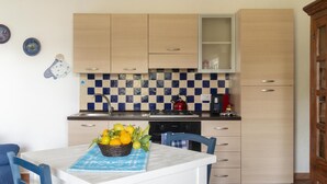 A compact kitchen with light wooden cabinets, a checkered backsplash, and a stove. A basket of lemons is on the counter. - Casa Oliveto 1 in Galtell (Galtelli)