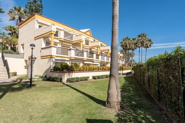 A multi-story hotel with balconies, a well-maintained lawn, and palm trees.