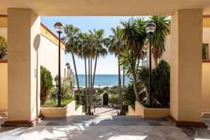 A corridor with a view of the ocean, palm trees, and a building entrance.