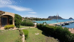 A coastal property with a stone archway, a grassy lawn, and a view of the sea with boats. - Welcomely - Villa Acqua Marina (Golfo Aranci)